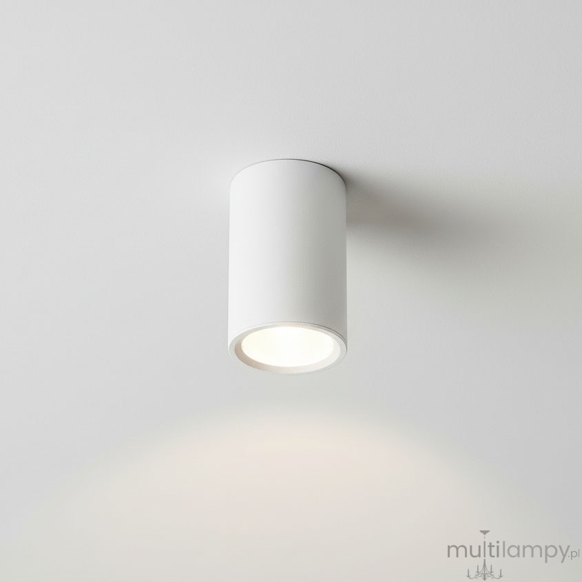 Boka lampa sufitowa w kształcie białej tuby, zamontowana na suficie, z miejscem na jedną żarówkę GU10. Widoczna jasna oprawa emitująca światło, z gładką, matową powierzchnią.
