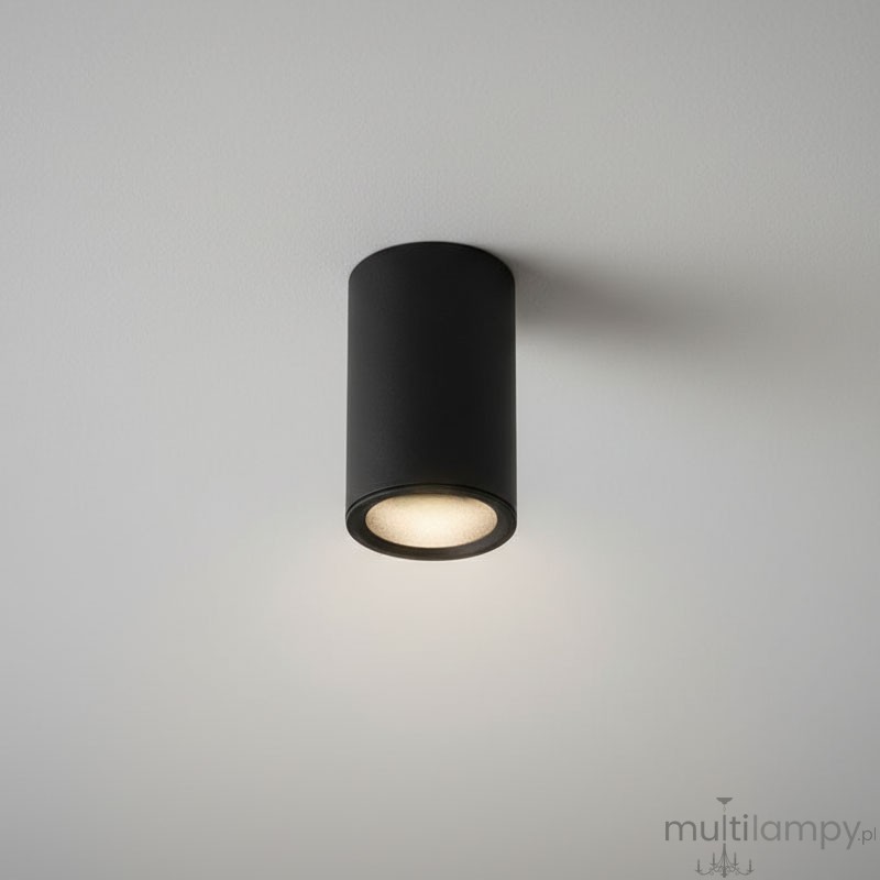 Czarna lampa sufitowa w kształcie tuby, zamontowana na białym suficie. Posiada jedno gniazdo GU10, emitujące ciepłe światło. Prosta, cylindryczna forma z matowym wykończeniem, idealna do nowoczesnych wnętrz.