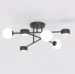 Lampa sufitowa Holon w kolorze czarnym z sześcioma źródłami światła G9/GX53. Posiada geometryczny kształt z trzema białymi kulami i trzema cylindrycznymi kloszami, zamontowana na okrągłej podstawie. Ujęcie z dołu, na jasnym tle.