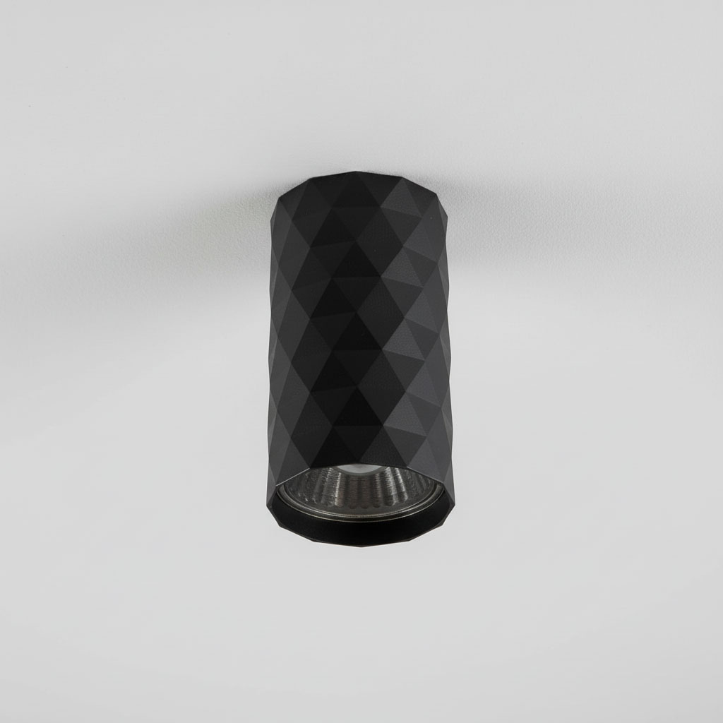 Czarna lampa sufitowa tuba GU10 o geometrycznym, diamentowym wzorze, zamontowana na białym suficie. Ujęcie frontalne, ukazujące detal wykończenia i otwór na źródło światła.