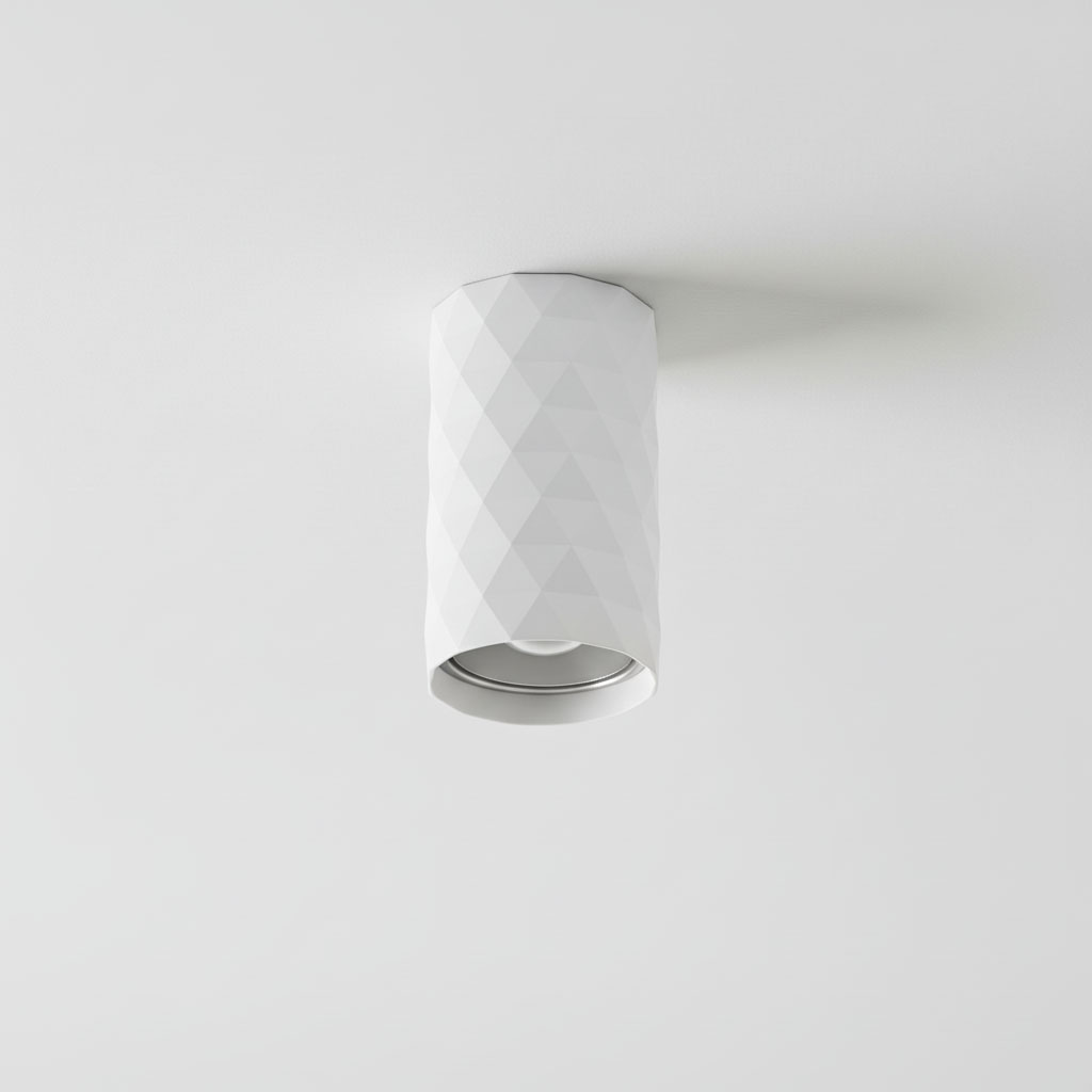 Biała lampa sufitowa tuba GU10 o cylindrycznym kształcie z wyraźnym, teksturowanym wzorem w diamenty. Zainstalowana na suficie, posiada okrągły otwór na żarówkę. Tło proste, jednolite, co podkreśla minimalistyczny design lampy.