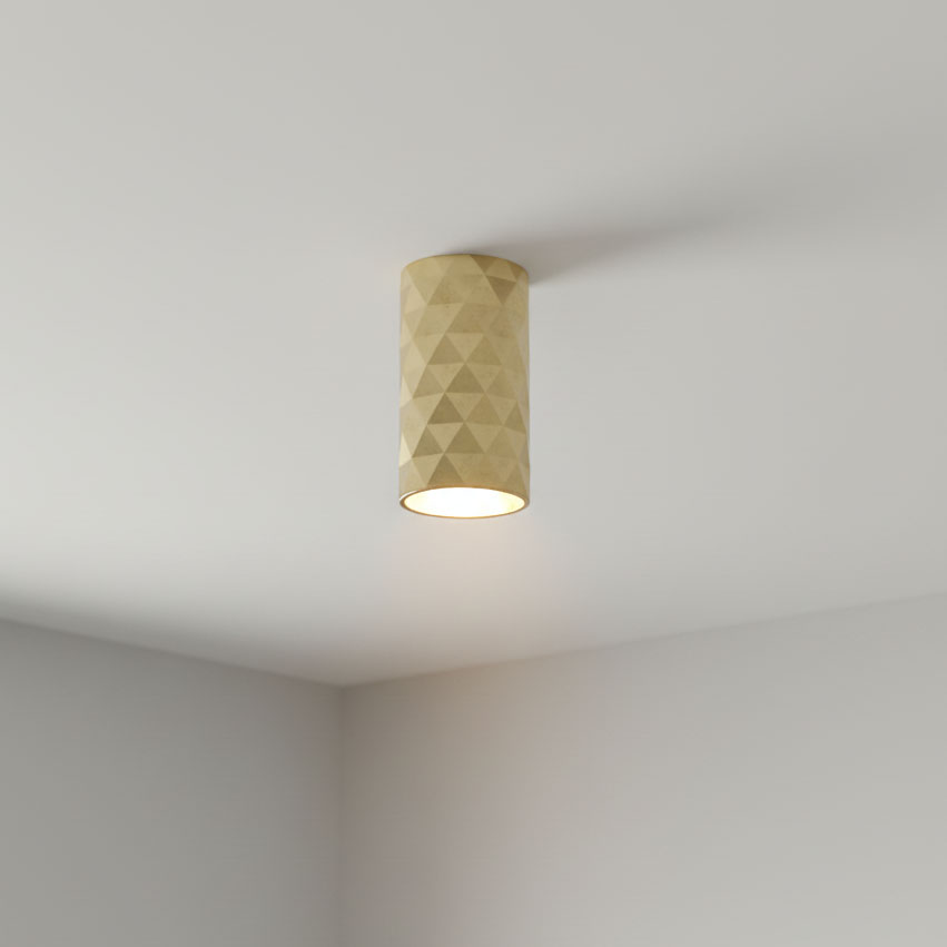 Złota lampa sufitowa w kształcie tuby z fakturą w formie diamentowych wzorów, zamontowana na białym suficie. Emituje światło z dolnej części, podkreślając nowoczesny design.
