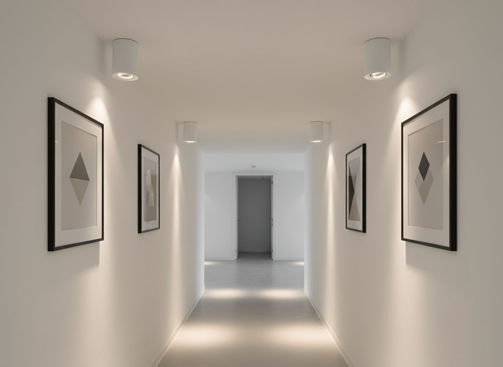 Biała lampa sufitowa tuba kierunkowa Devo z jedną oprawą GU10, zamontowana na suficie w wąskim korytarzu. Oświetlenie skierowane na ściany z minimalistycznymi obrazami w ramkach, na jasnym tle.