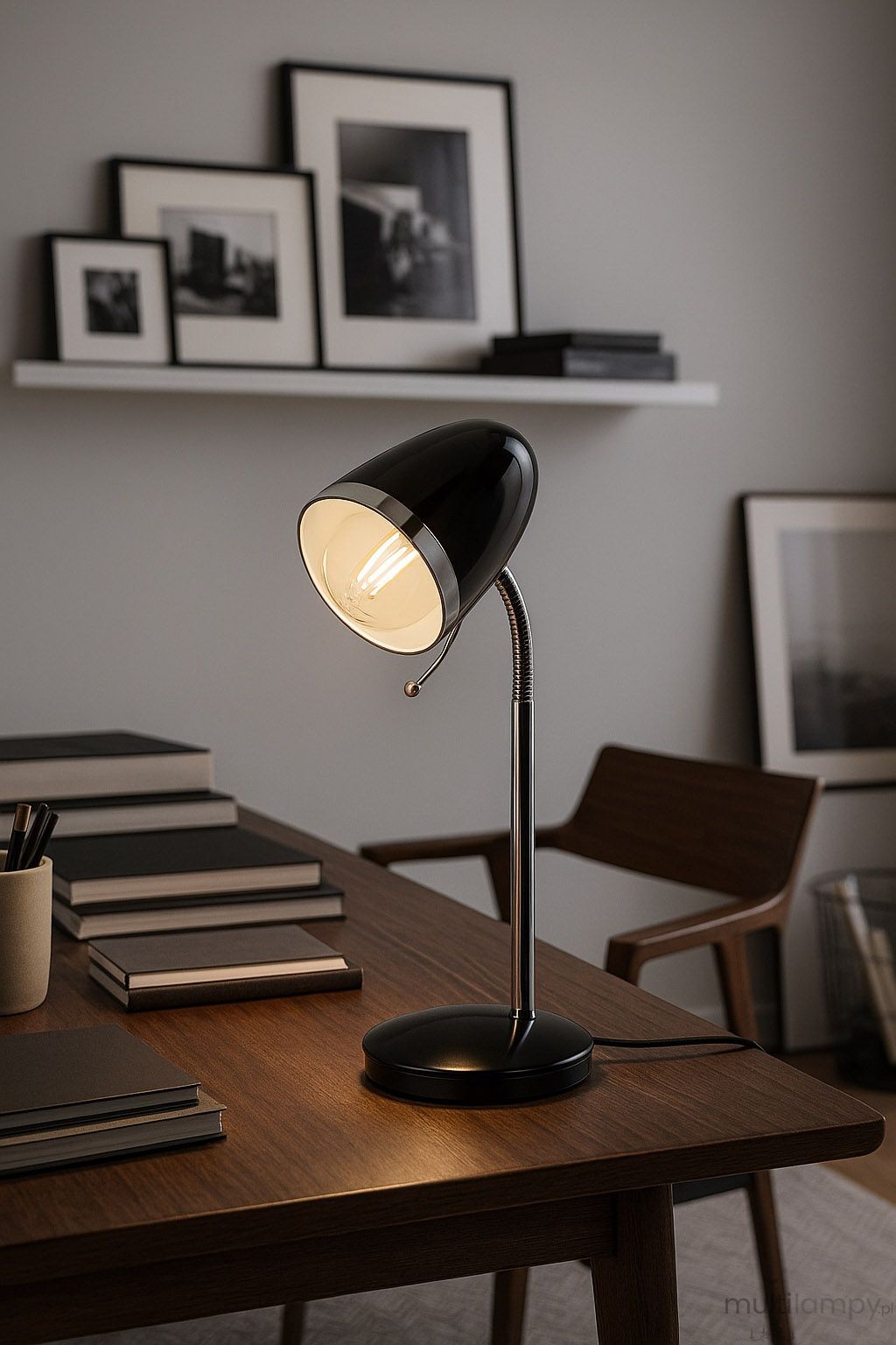 Lampka biurkowa Kajtek w kolorze czarnym z metalowym, elastycznym ramieniem i okrągłą podstawą. Widoczna żarówka E27, na drewnianym biurku w minimalistycznym wnętrzu z książkami i dekoracjami w tle.