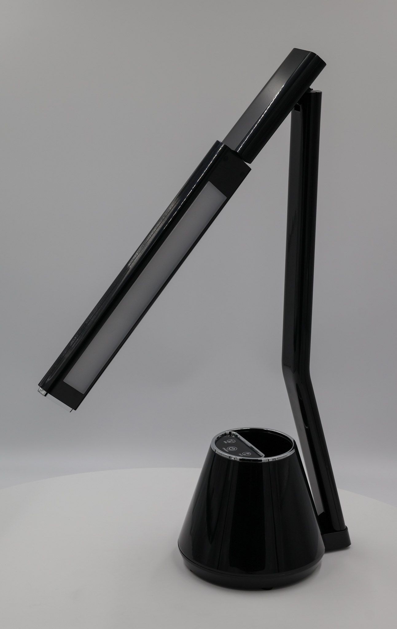 Czarna lampka biurkowa Kiki z LED 8W, z regulowanym ramieniem. Kształt stożkowaty u podstawy z panelem sterującym. Wysoka, smukła konstrukcja z matowym wykończeniem, stojąca na białym tle.