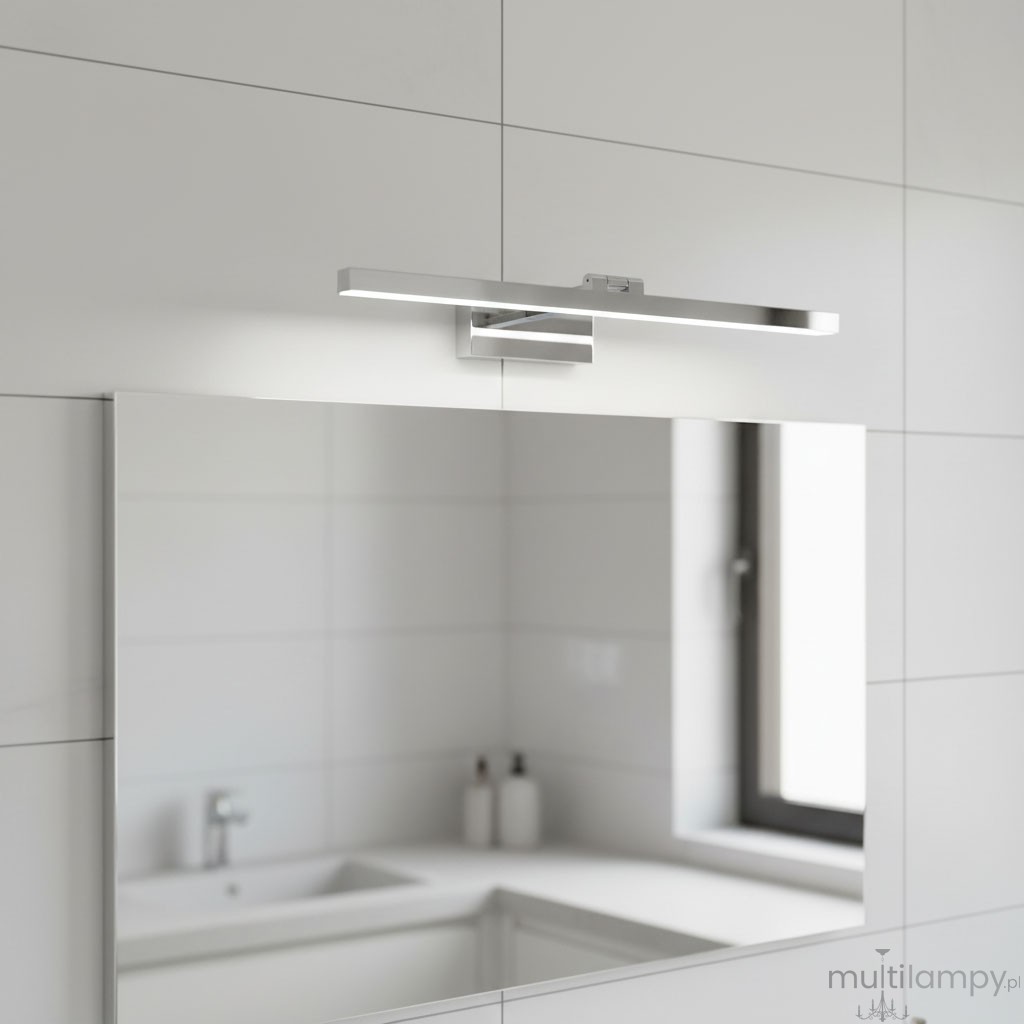 Kinkiet łazienkowy LED Lappa w kolorze chromu, zamontowany nad lustrem. Posiada prostokątny kształt i minimalistyczny design, emitując jasne światło, w otoczeniu jasnych płytek ceramicznych i białego blatu umywalki.