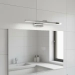 Kinkiet łazienkowy LED Lappa w kolorze chromu, zamontowany nad lustrem. Posiada prostokątny kształt i minimalistyczny design, emitując jasne światło, w otoczeniu jasnych płytek ceramicznych i białego blatu umywalki.
