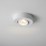 Ruchoma oprawa podtynkowa Beta w białym kolorze, okrągła z gładką powierzchnią, z widoczną żarówką w środku, zamontowana w suficie. Oświetlenie skierowane w dół, na jednolitym, jasnym tle.