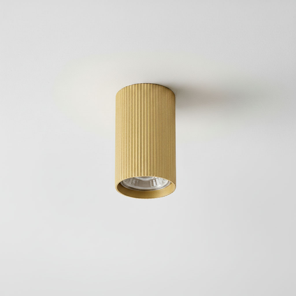 Lampa sufitowa Lucerno w kształcie tuby, w kolorze złotym, z żłobioną fakturą. Ujęcie frontalne, zamontowana na białym suficie. Widoczna oprawa żarówki GU10.