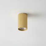 Lampa sufitowa Lucerno w kształcie tuby, w kolorze złotym, z żłobioną fakturą. Ujęcie frontalne, zamontowana na białym suficie. Widoczna oprawa żarówki GU10.