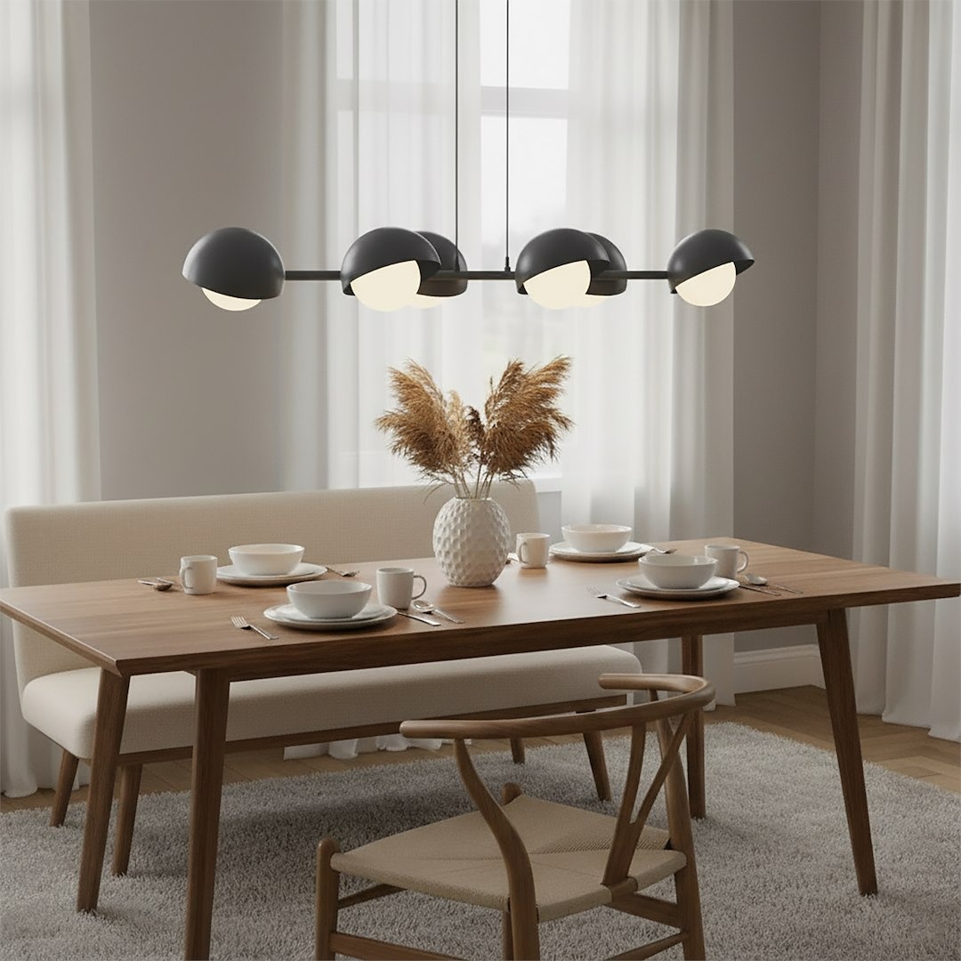 Lampa wisząca Boom 6xG9 w kolorze czarnym, z sześcioma okrągłymi kloszami w białym i czarnym odcieniu, zawieszona nad drewnianym stołem. W tle widoczne zasłony i dekoracje, w tym wazon z suchymi kwiatami oraz zastawa stołowa.
