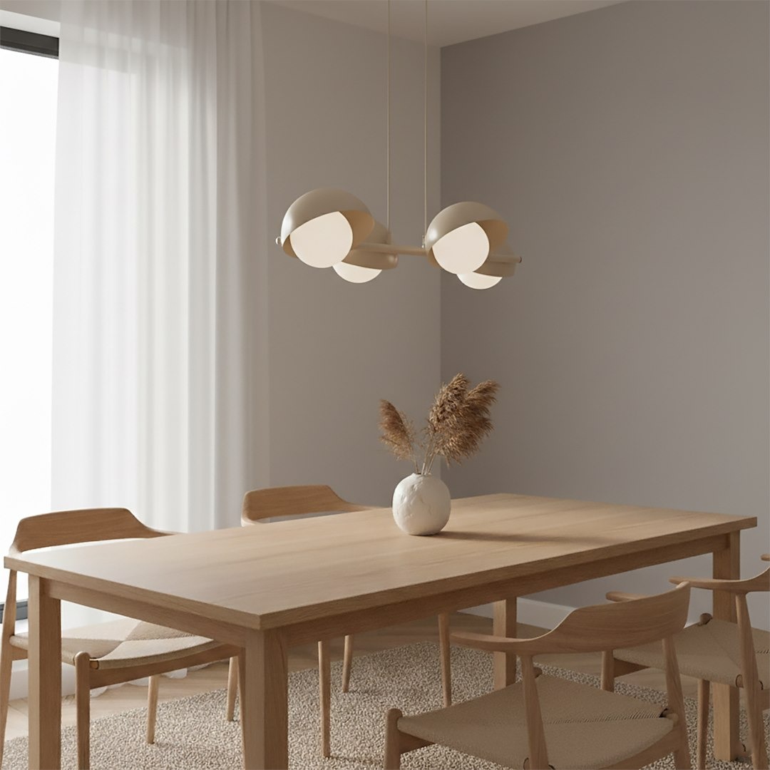 Lampa wisząca Boom 4xG9 w kolorze mokka, z okrągłymi kloszami, zawieszona na długich kablach. Umieszczona nad drewnianym stołem w jasnym wnętrzu z szarymi ścianami i roślinnym akcentem w wazonie.