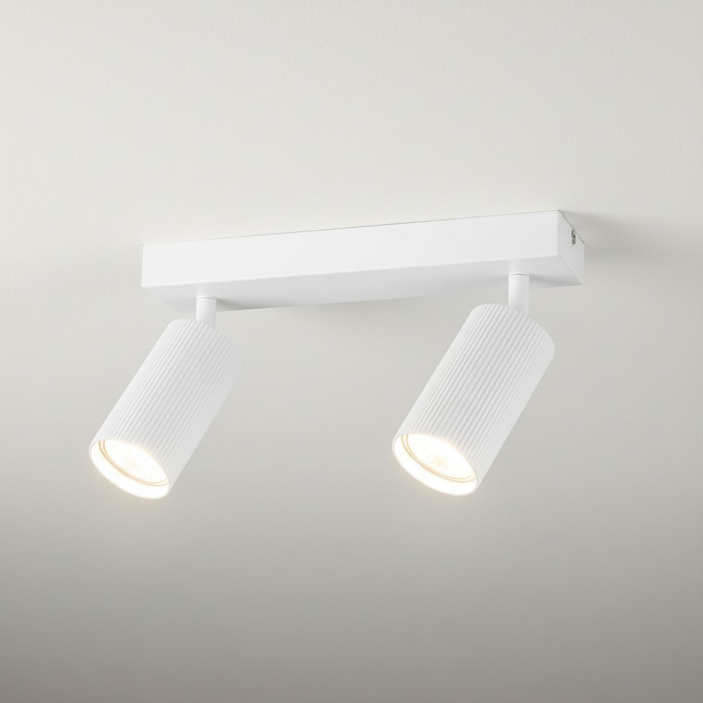 Biała lampa sufitowa Lucerno z dwoma reflektorami na regulowanych ramionach. Cylindryczne klosze o teksturowanej powierzchni, zamontowane na prostokątnej podstawie. Oświetlenie w minimalistycznym stylu, idealne do nowoczesnych wnętrz.