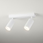 Biała lampa sufitowa Lucerno z dwoma reflektorami na regulowanych ramionach. Cylindryczne klosze o teksturowanej powierzchni, zamontowane na prostokątnej podstawie. Oświetlenie w minimalistycznym stylu, idealne do nowoczesnych wnętrz.