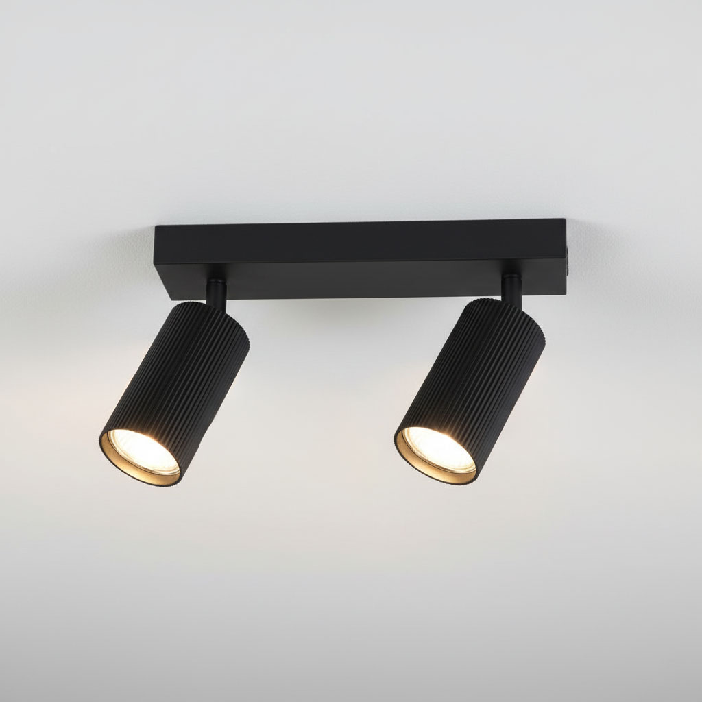 Czarna lampa sufitowa Lucerno z dwoma reflektorami GU10, umieszczona na prostokątnej podstawie. Reflektory mają teksturowaną powierzchnię, skierowane w dół. Lampa montowana do sufitu, na jasnym tle.