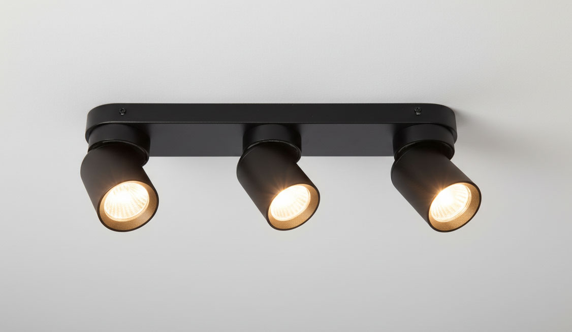 Czarna lampa sufitowa Timo, 3-punktowa, z trzema regulowanymi spotami. Ujęcie z dołu, ukazujące zamontowaną lampę na białym suficie. Każdy spot ma okrągłą, metalową podstawę z widocznymi żarówkami emitującymi światło.