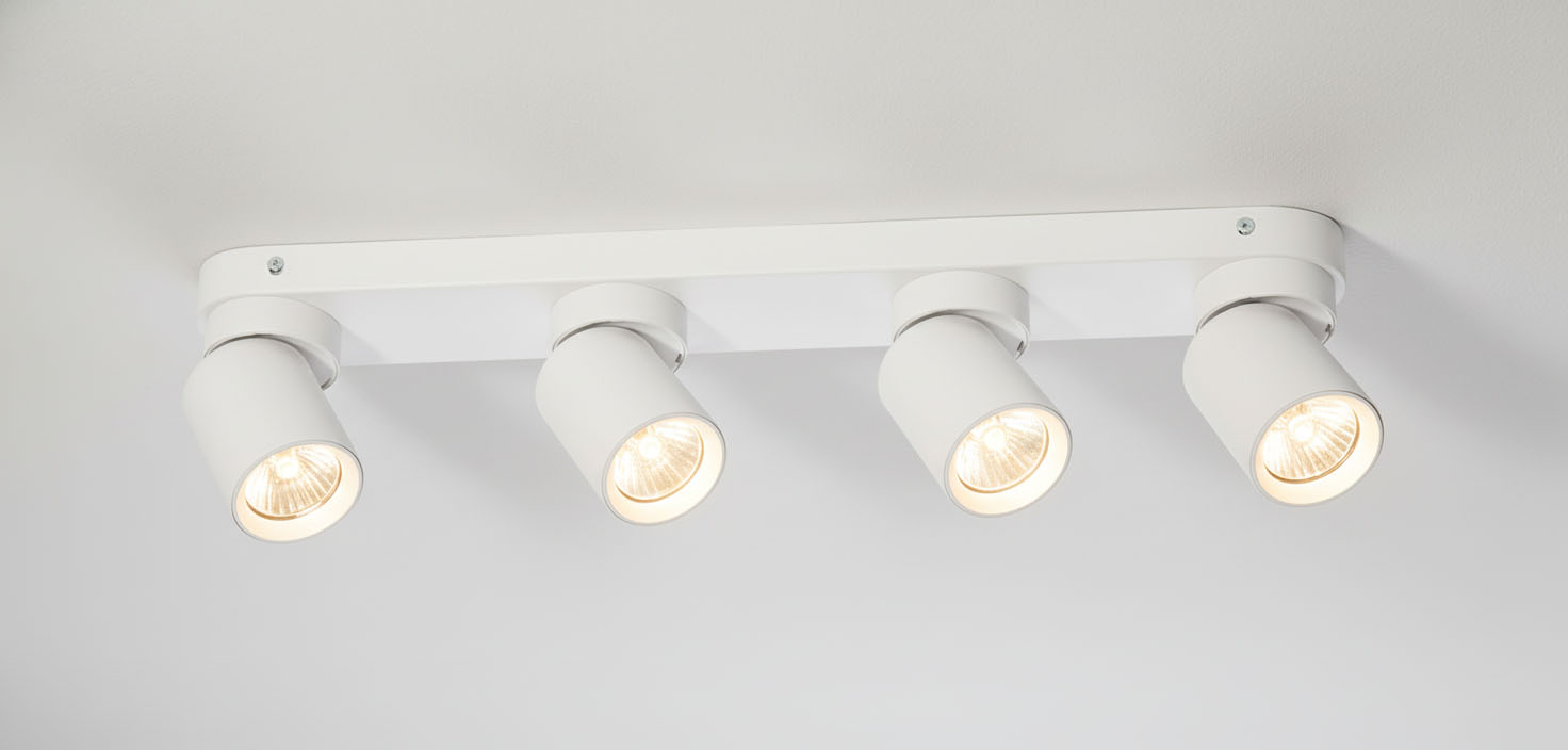 Lampa sufitowa Timo, 4-punktowa, w kolorze białym. Ułożona poziomo, z czterema ruchomymi reflektorami o cylindrycznym kształcie. Każdy reflektor ma szklaną oprawę, emitującą ciepłe światło. Montaż na suficie, minimalistyczny design.