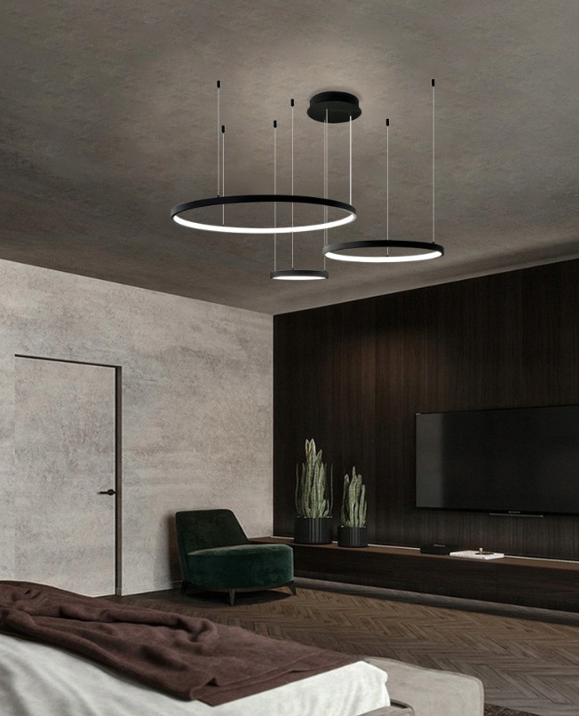 Lampa wisząca LED Hodo w kolorze czarnym z trzema okrągłymi elementami o średnicach 20, 40 i 60 cm, zawieszona na cienkich linkach. Pilot do zdalnego sterowania. Zainstalowana w nowoczesnym wnętrzu z drewnianą podłogą i ciemnym tłem.