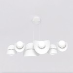 Lampa wisząca Elementi 6xG9 w białym kolorze, składająca się z pięciu asymetrycznych kloszy z zaokrąglonymi krawędziami i okrągłymi żarówkami. Zawieszona na białych linkach, montowana na suficie. Tło jednolite, jasne.