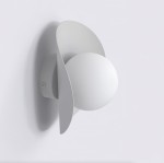 Kinkiet Fiero M w kolorze szarym, z okrągłą, białą oprawą i ozdobnymi, falistymi elementami. Montowany na ścianie, z widocznym mocowaniem. Lampa przeznaczona do żarówki G9.