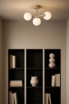 Beżowa lampa sufitowa Ardi z trzema okrągłymi, mlecznymi kloszami umieszczonymi na metalowym stelażu. Produkt montowany na suficie, widoczny w minimalistycznym wnętrzu z ciemnymi regałami i dekoracjami.