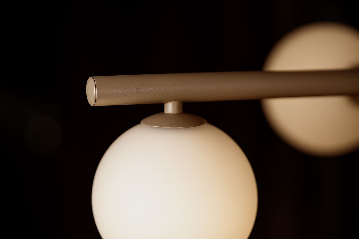 Beżowa lampa wisząca Ardi z dziewięcioma oprawami G9. Zbliżenie na metalowy uchwyt i matową, szklaną kulę, która emituje subtelne światło. Lampa zawieszona w poziomie na ciemnym tle, podkreślająca nowoczesny design.