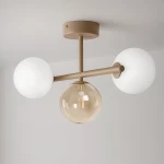 Beżowa lampa sufitowa Lemo z trzema źródłami światła: dwa białe, matowe klosze w formie kul oraz jeden szklany, przezroczysty klosz. Ujęcie z dołu, produkt zamontowany na suficie. Metalowa konstrukcja w odcieniu beżowym.