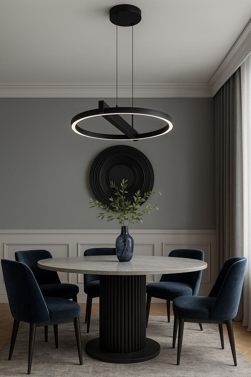Lampa wisząca Tivoli 1xLED 24W CCT w kolorze czarnym, o okrągłym kształcie, zawieszona na cienkich linkach. Wyposażona w pierścień świetlny, umieszczona nad okrągłym stołem w jadalni, w otoczeniu niebieskich krzeseł i dekoracyjnej wazonu z roślinami.