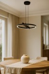 Lampa wisząca Tivoli w kolorze czarnym z okrągłym kloszem LED 24W CCT. Zawieszona na dwóch cienkich linkach, z widocznym włącznikiem w kształcie krzyża. Produkt w nowoczesnym wnętrzu, nad drewnianym stołem z dekoracyjnym wazonem.