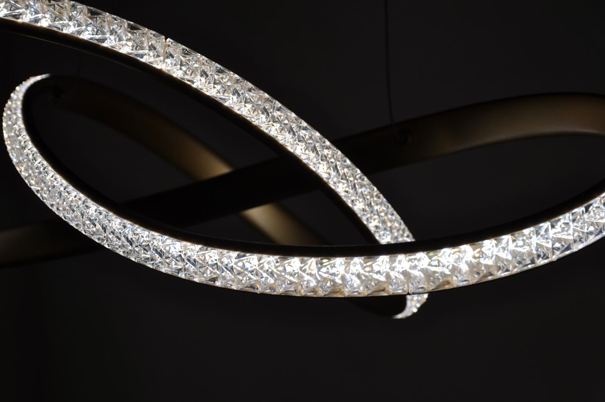 Złota lampa wisząca Fondi K-8237 z jedną diodą LED 40W, o nowoczesnym, spiralnym kształcie. Wykończenie z przezroczystymi kryształkami, które odbijają światło, wisząca w ciemnym tle, w zbliżeniu na detale.