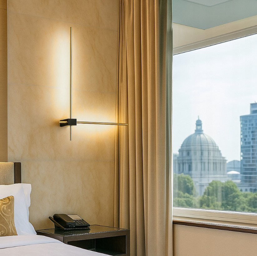 Kinkiet LED Como 2x60, z metalowym czarnym korpusem i złotymi akcentami, zamontowany na ścianie. Emituje chłodne, białe światło (4000K). W tle widoczna zasłona i okno z panoramicznym widokiem na miasto.