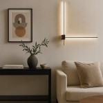 Kinkiet LED Como 2x60 z dwoma źródłami światła, o mocy 12W i barwie 4000K, w kolorze złotym i czarnym. Montowany na ścianie, z minimalistycznym designem, umieszczony obok sofy w nowoczesnym wnętrzu.