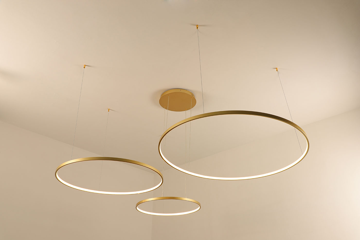 Lampa wisząca LED Hodo w kolorze złotym, z trzema okrągłymi pierścieniami o średnicach 40, 60 i 80 cm. Zamontowana na suficie, z widocznymi przewodami. Design minimalistyczny, z możliwością zdalnego sterowania za pomocą pilota.