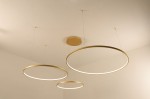 Lampa wisząca LED Hodo w kolorze złotym, z trzema okrągłymi pierścieniami o średnicach 40, 60 i 80 cm. Zamontowana na suficie, z widocznymi przewodami. Design minimalistyczny, z możliwością zdalnego sterowania za pomocą pilota.