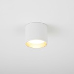 Lampa sufitowa Golda w formie białej tuby z złotym wnętrzem, zamontowana na białym suficie. Wnętrze lampy emituje światło, tworząc kontrast między białą a złotą powierzchnią. Prosty, cylindryczny kształt, do zastosowania w nowoczesnych wnętrzach.