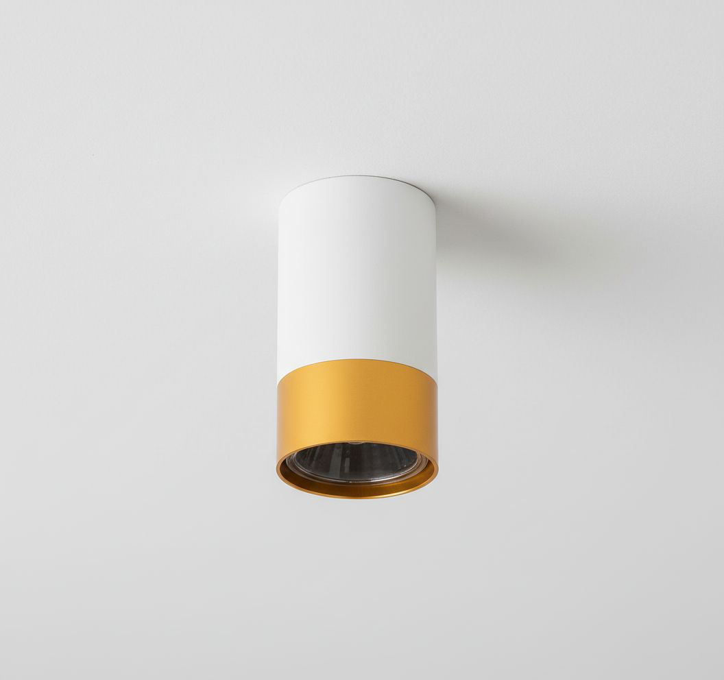 Lampa sufitowa Klemens w kształcie tuby, z białym korpusem i złotym detalem na dole. Zainstalowana na suficie, z miejscem na żarówkę GU10. Proste, nowoczesne wzornictwo, idealna do różnych aranżacji wnętrz.