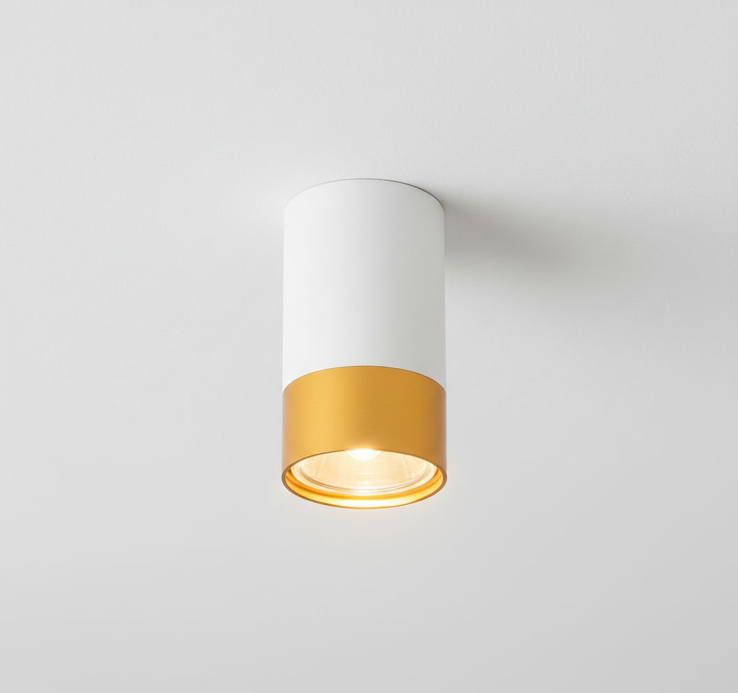 Lampa sufitowa Klemens w kształcie tuby, z białym korpusem i złotym wykończeniem u dołu. Ujęcie z dołu, pokazujące widoczne źródło światła GU10. Produkt zamontowany na białym suficie, w minimalistycznym stylu.