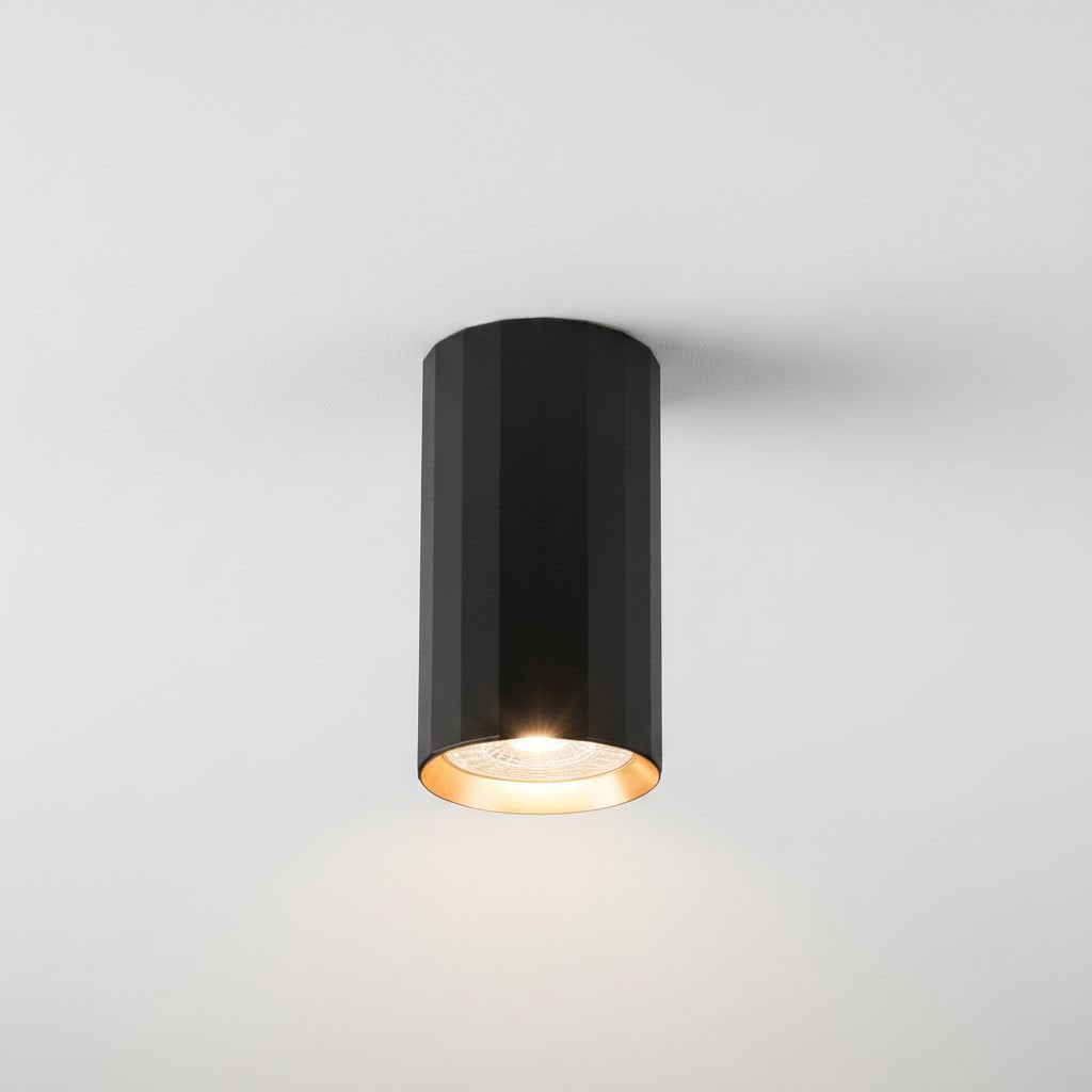 Czarna lampa sufitowa w kształcie tuby z wykończeniem w kolorze złotym. Widoczna z przodu, montowana na suficie, z widocznym źródłem światła GU10. Gładka powierzchnia i cylindryczny kształt podkreślają nowoczesny design.