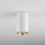 Lampa sufitowa Nicea w kształcie tuby, biała z złotym wykończeniem. Posiada strukturę z rowkami, zainstalowany gwint GU10 na dole. Ujęcie frontalne, zamontowana na suficie, idealna do nowoczesnych wnętrz.