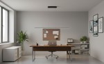 Lampa wisząca Kiki w kolorze czarnym, z jedną diodą LED o mocy 20W. Zawieszona równolegle nad biurkiem w nowoczesnym wnętrzu biurowym, z metalową konstrukcją i minimalistycznym designem. Tło jasnoszare, z oknem i roślinnością.