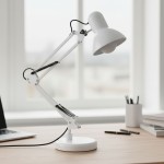 Biała lampka biurkowa Lena z regulowanym ramieniem, uchwytem do stołu i podstawą. Widoczne elementy to klosz w kształcie stożka oraz sprężynowe mocowania. Ujęcie z boku na stole, w tle laptop i przybory biurowe.
