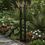 Lampa stojąca ogrodowa Santina LED H80 w antracytowym kolorze, o prostokątnym kształcie, umieszczona w ogrodzie, otoczona zielonymi roślinami i kolorowymi kwiatami. Ujęcie z boku, pokazujące elegancki design i wysokość lampy.