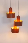 Lampa wisząca Rif w kolorze ceglastym z trzema źródłami światła E27. Produkt zawiera okrągłe klosze o matowej fakturze, zawieszone na cienkich przewodach. Ujęcie z przodu, ukazujące harmonijną kompozycję.