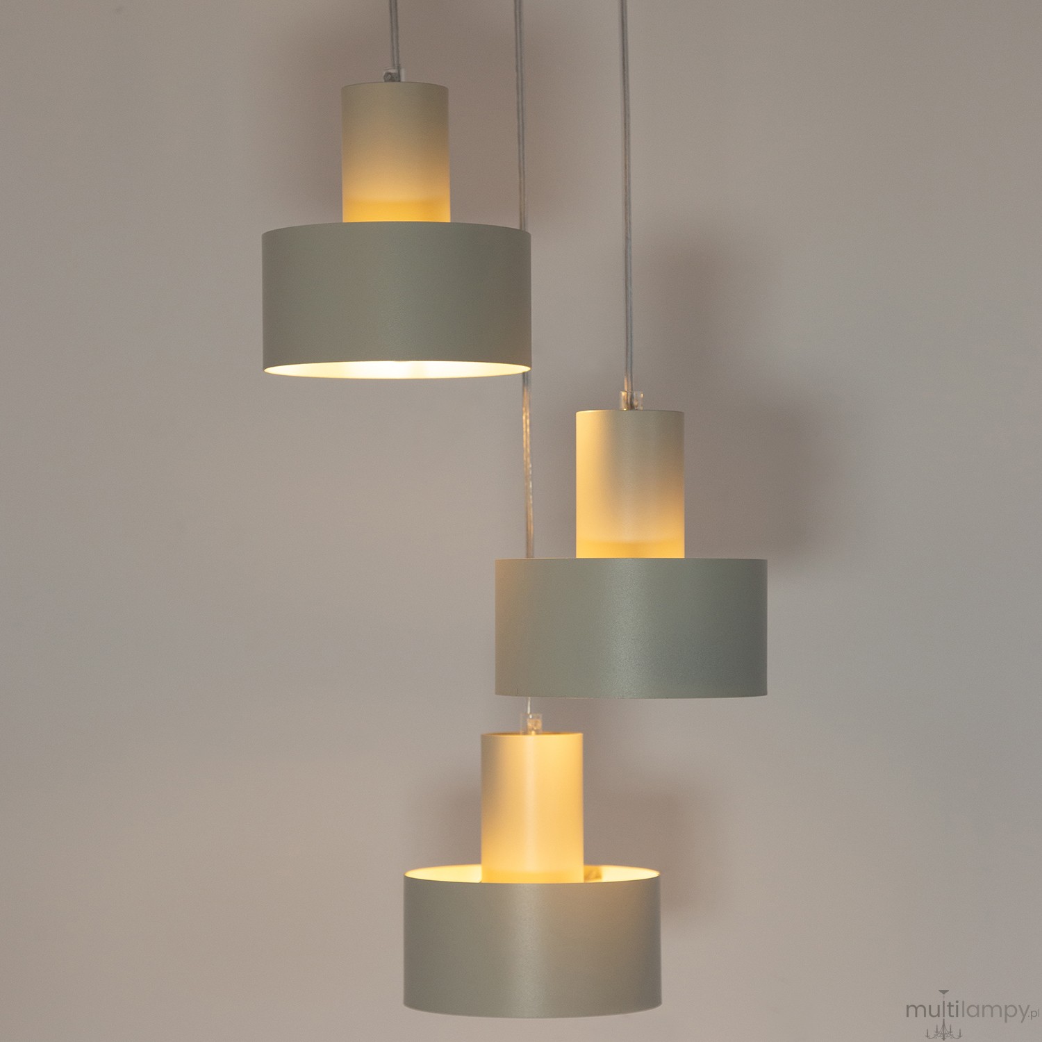 Lampa wisząca Rif w szarym beżu z trzema oprawami E27, zawieszona na trzech kablach. Składa się z dwóch cylindrycznych, matowych kloszy oraz jednego klosza w przezroczystym wykończeniu, emitującego ciepłe światło.
