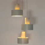 Lampa wisząca Rif w szarym beżu z trzema oprawami E27, zawieszona na trzech kablach. Składa się z dwóch cylindrycznych, matowych kloszy oraz jednego klosza w przezroczystym wykończeniu, emitującego ciepłe światło.