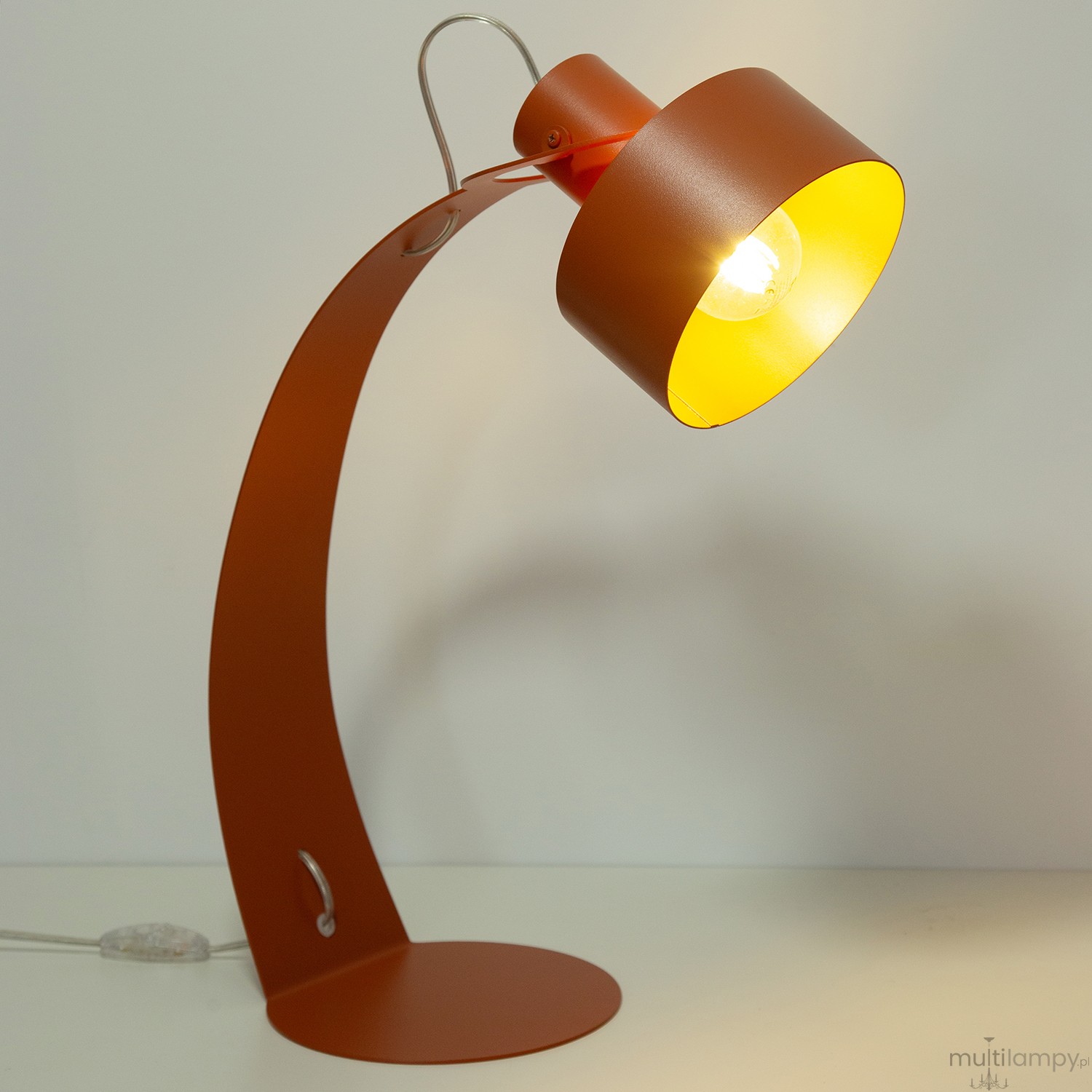 Lampa stołowa Rif z ceglaną podstawą, z metalowym kloszem w ciepłym odcieniu żółtym. Ustawiona w pozycji stojącej, z zagiętą nogą i przewodem z włącznikiem. Widoczny detal uchwytu na kloszu. Tło jasne, proste.