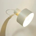 Lampa stołowa Rif z metalowym kloszem w odcieniu szaro-beżowym, z jednym źródłem światła E27. Ujęcie z góry, zbliżenie na klosz i mocowanie. Kształt zaokrąglony, z widocznym drucikiem mocującym.