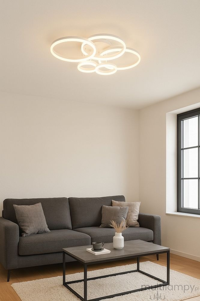 Lampa sufitowa Ravello z pięcioma okrągłymi źródłami LED o mocy 70W w białym kolorze, zawieszona na suficie w jasnym wnętrzu. Okręgi różnej wielkości tworzą nowoczesny design. W tle widoczna kanapa i stół.