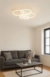 Lampa sufitowa Ravello z pięcioma okrągłymi źródłami LED o mocy 70W w białym kolorze, zawieszona na suficie w jasnym wnętrzu. Okręgi różnej wielkości tworzą nowoczesny design. W tle widoczna kanapa i stół.