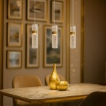 Lagos lampa wisząca LED 24W 4000K w złotym kolorze, z przezroczystym kloszem i geometrycznym wzorem, zawieszona nad stołem na marmurowym blacie, w eleganckim wnętrzu z obrazami w tle.